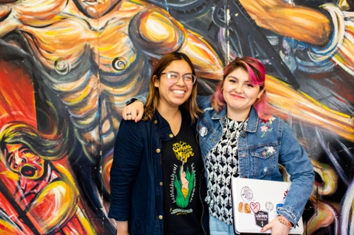 Two female students stand in front of a mural