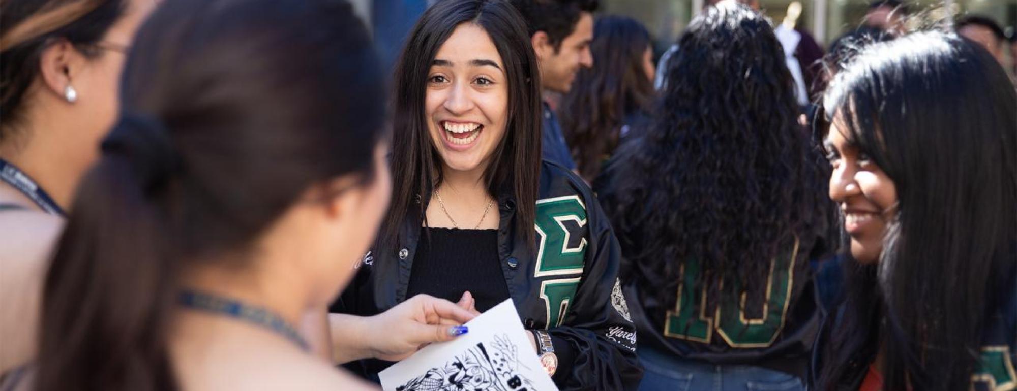 Female students in a group smiling with one of them holding a drawing that says "Bienvenida"