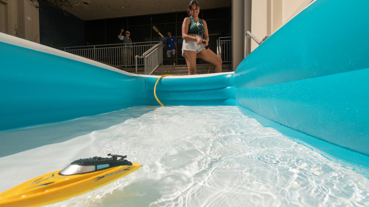 A toy boat in an inflatable pool with a person controlling it nearby.