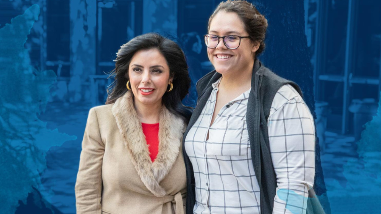 Two women of diverse backgrounds stand together smiling