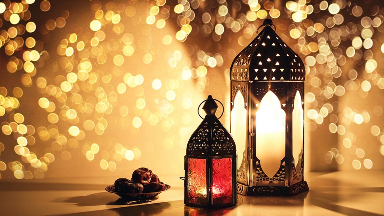 two lanterns on table with a small apple beside it. background is of golden twinkling lights