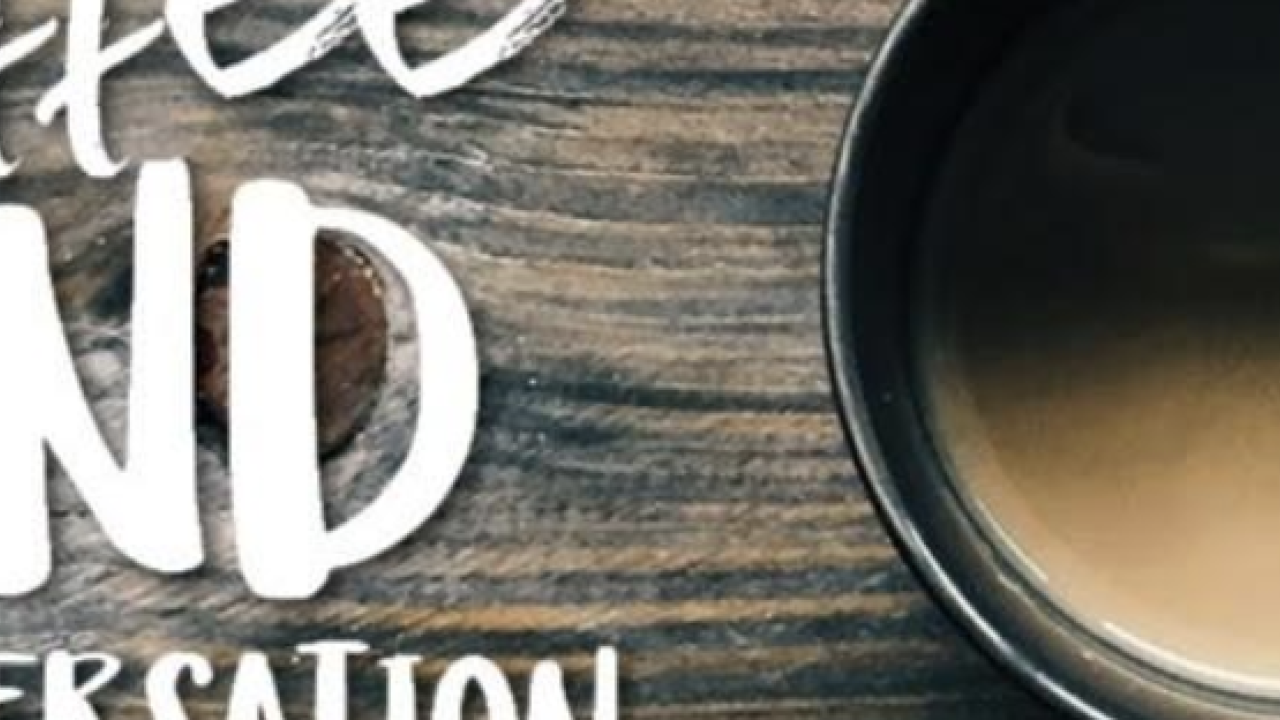 Cup of coffee on a wooden table with text reading "Coffee and Conversation."