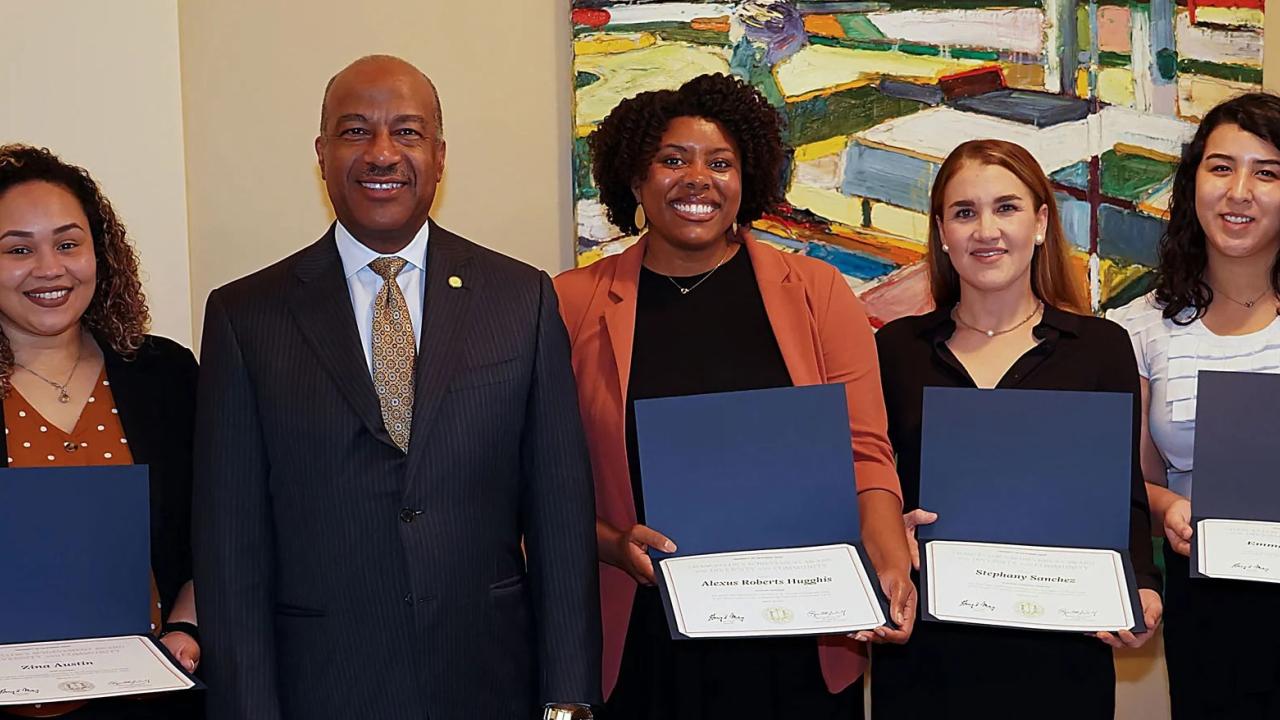 Five people posing with certificates in front of an abstract painting.