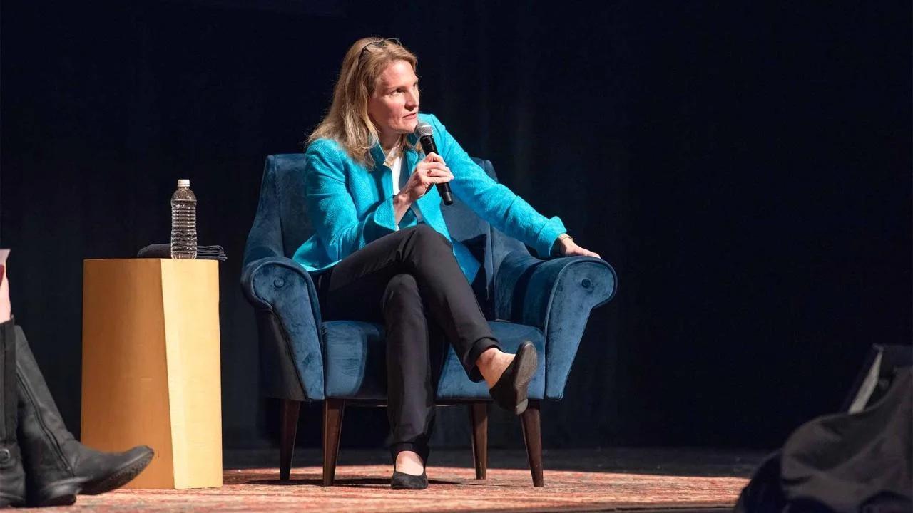 Cynthia Miller-Idriss speaks at the Mondavi Center on Feb. 5. She is seated in a blue chair on stage and is wearing a bright teal coat and black pants and is speaking into a microphone.