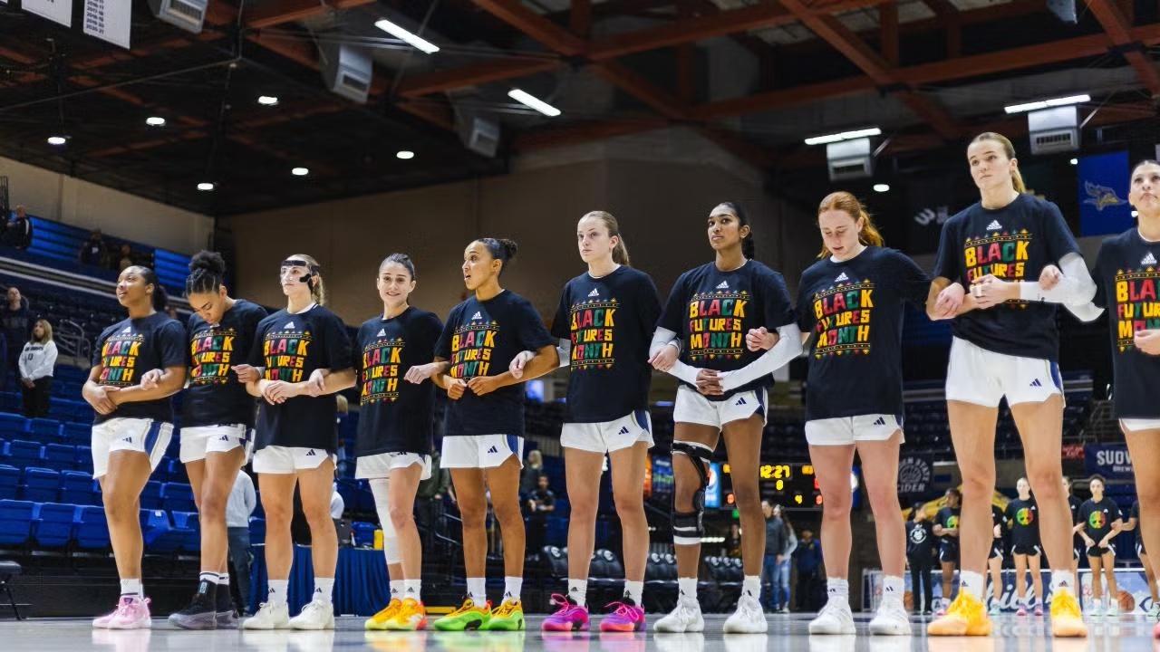 womens basketball team stand side by side with arms linked. they are all wearing a tshirt that says black futures month