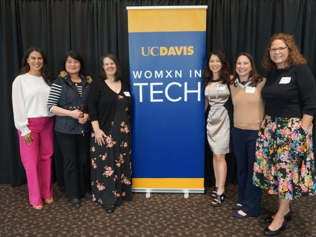six women stand with Womxn in Tech banner
