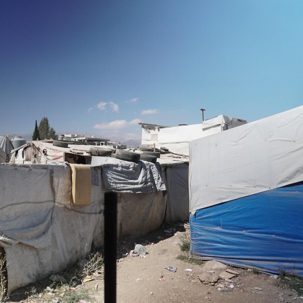 A makeshift settlement with tents made of white and blue tarps under a clear sky.