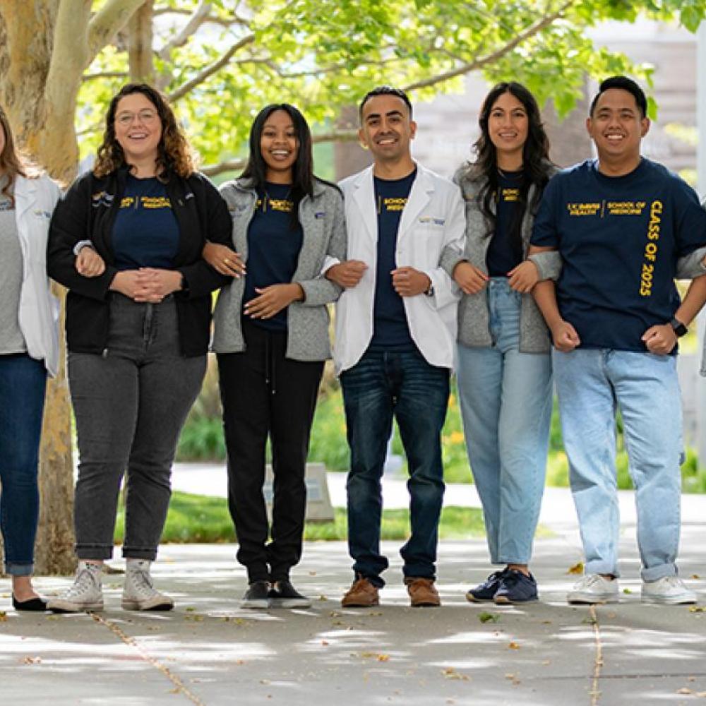 A group of people standing in a line under trees, wearing lab coats and casual clothing.