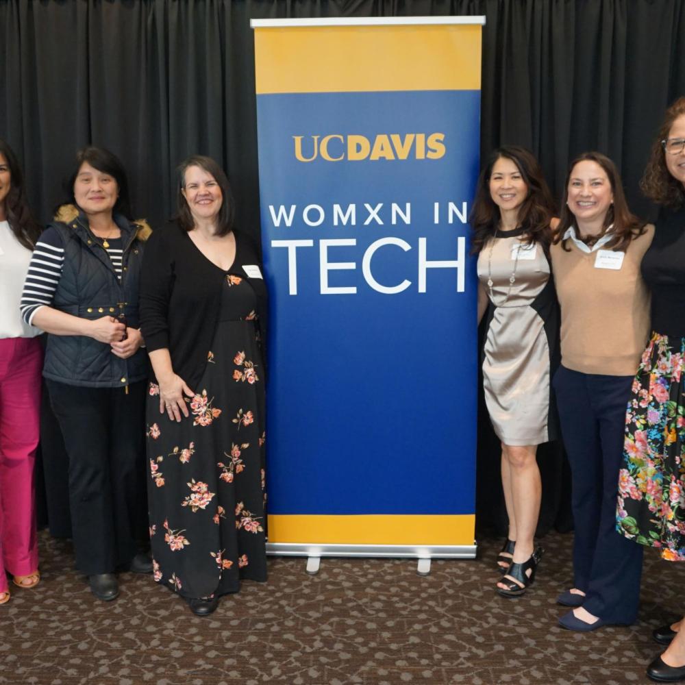 six women stand with Womxn in Tech banner