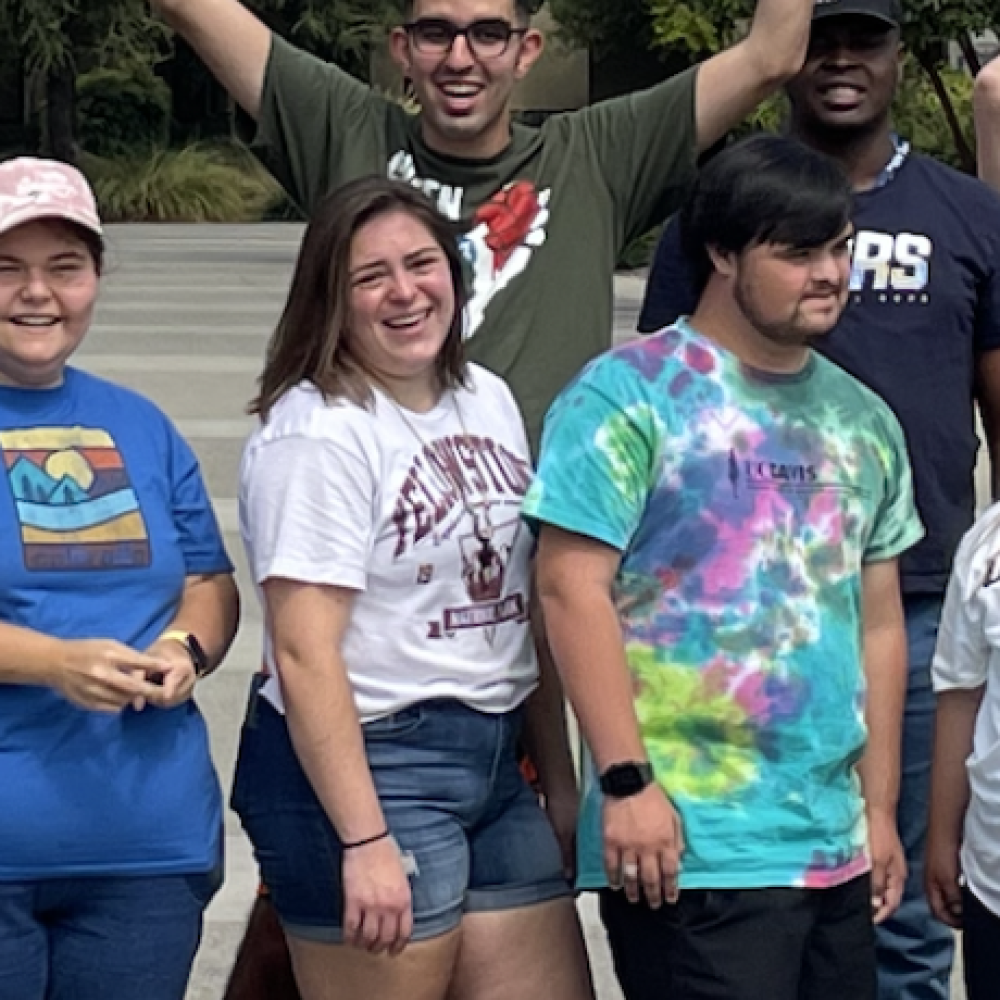 A group of students outside with their arms up, smiling.