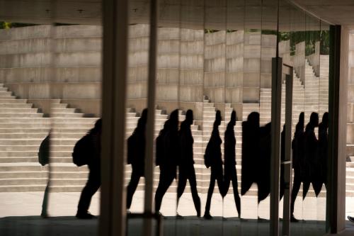 Reflections of people walking, distorted in a mirrored building surface with a background of concrete steps and walls.