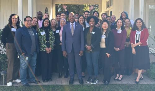 A group of UC Davis faculty and staff pose for a photo with Chancellor Gary S. May during the 2025 AAC/ERG Breakfast. The group stands smiling outdoors in front of a white building with columns, wearing name tags and business or business-casual attire.