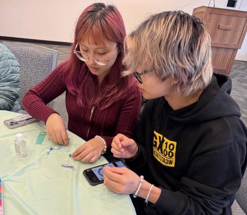 two students sit at table making bracelets at de-stress event