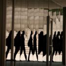 Reflections of people walking, distorted in a mirrored building surface with a background of concrete steps and walls.