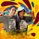 Two smiling individuals wearing "UC DAVIS ARBORETUM AND PUBLIC GARDEN" t-shirts and purple gloves against a colorful abstract background.