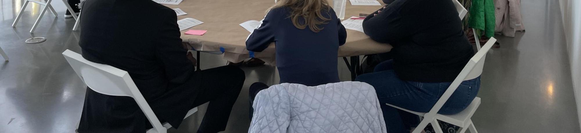 Groups of people sitting at round tables and in conversation with someone speaking near a white board
